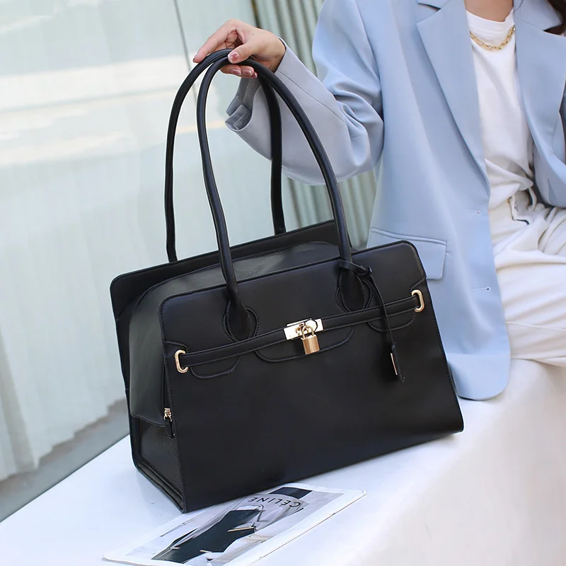 Black handbag held by a person wearing a light blue blazer and white pants, with a magazine underneath.