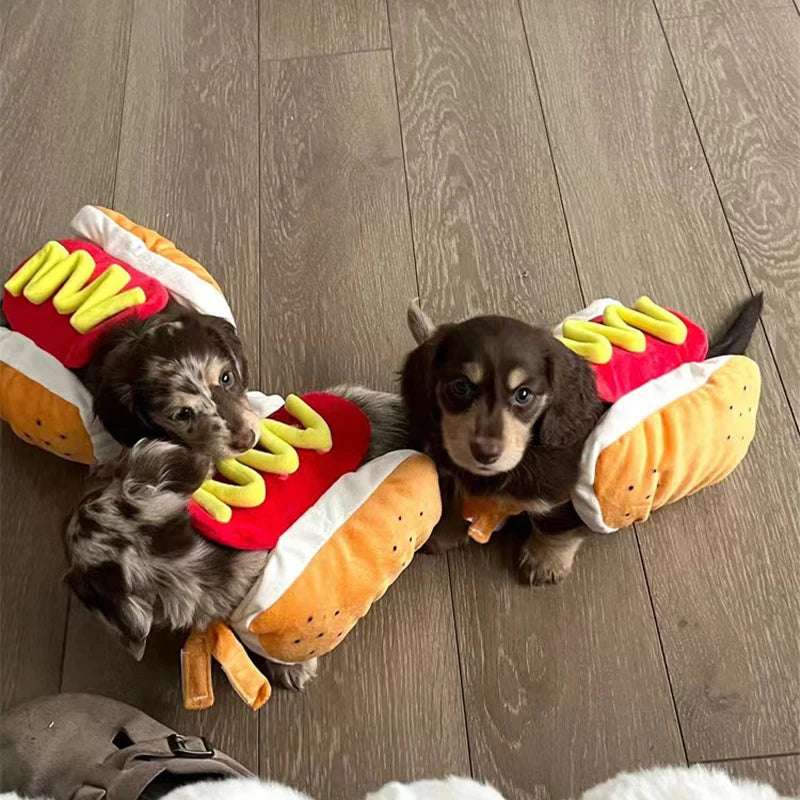 Two small dogs wearing hot dog-themed slippers on a wooden floor.
