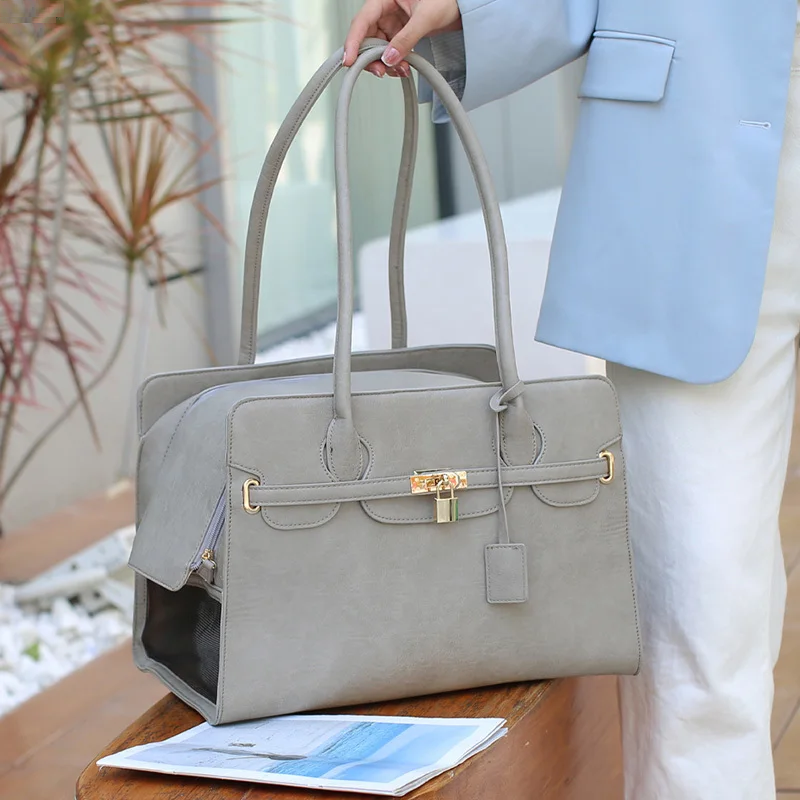 Gray handbag with gold accents held by a person in a light blue jacket and white pants.