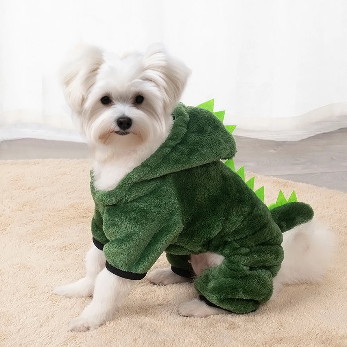 Small white dog wearing a green dinosaur costume on a beige carpet.